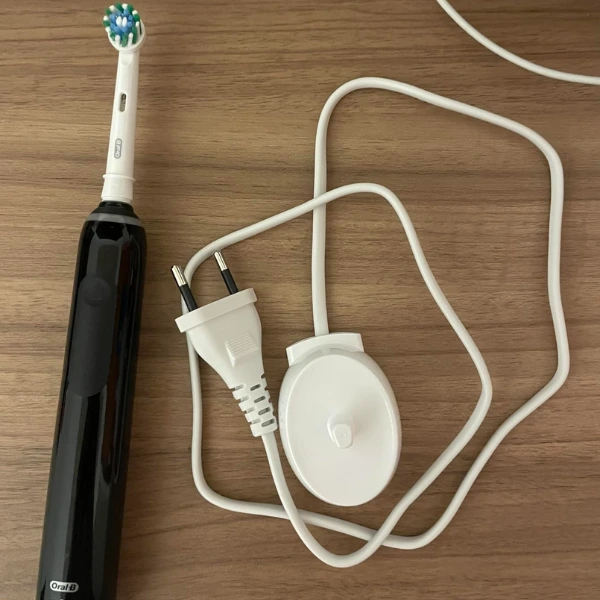 Escova elétrica Oral-B PRO Series 3 ao lado do carregador com cabo enrolado sobre superfície de madeira