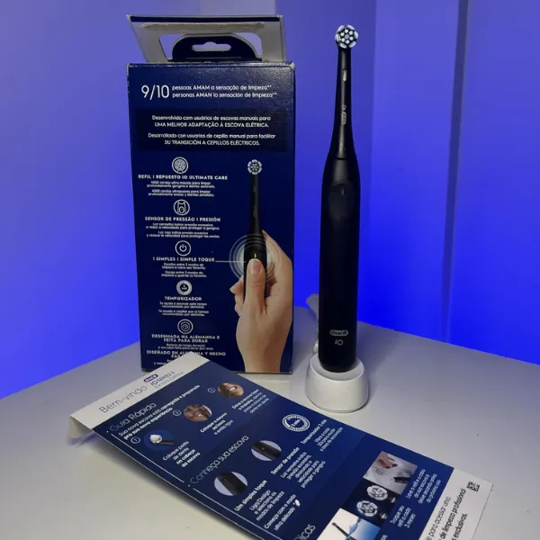 Escova elétrica Oral-B iO Series 2 apoiada na base em frente à caixa aberta e folheto de boas-vindas em fundo iluminado