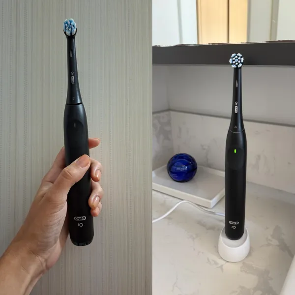 Escova elétrica Oral-B iO Series 2 sendo segurada na mão e apoiada na base carregadora em bancada de banheiro