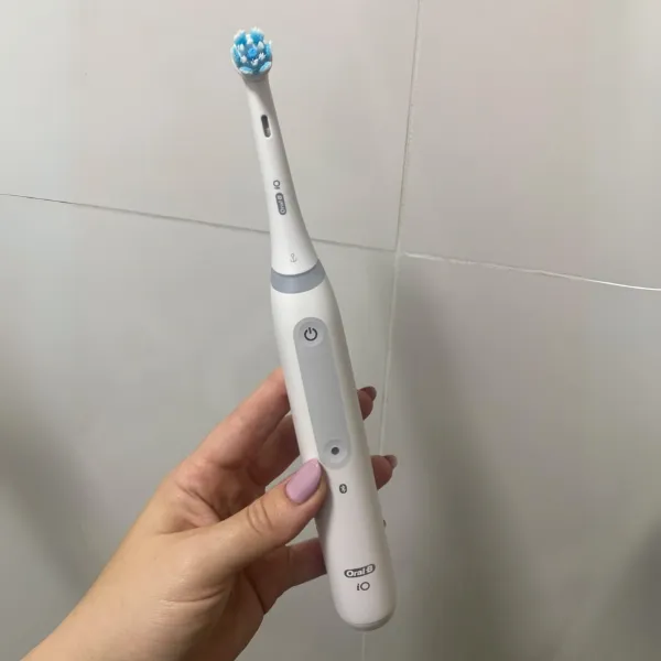 Pessoa segurando a escova Oral-B iO Series 4 com detalhes do botão de controle e corpo branco