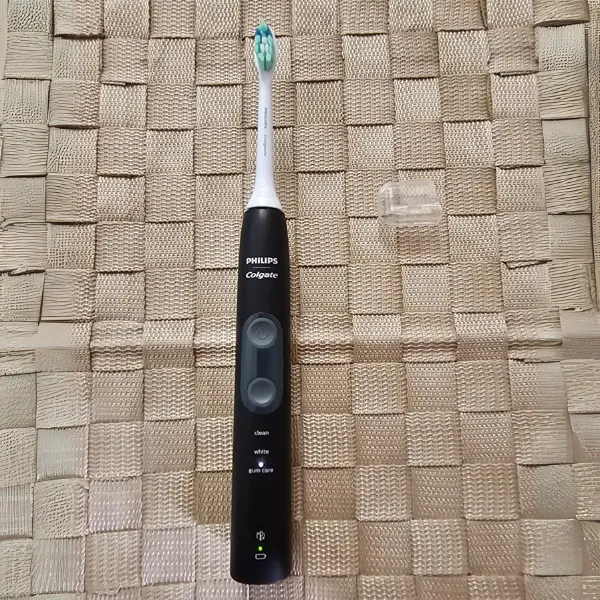 Escova elétrica Philips Colgate SonicPro 50 com corpo preto sobre superfície de palha sintética