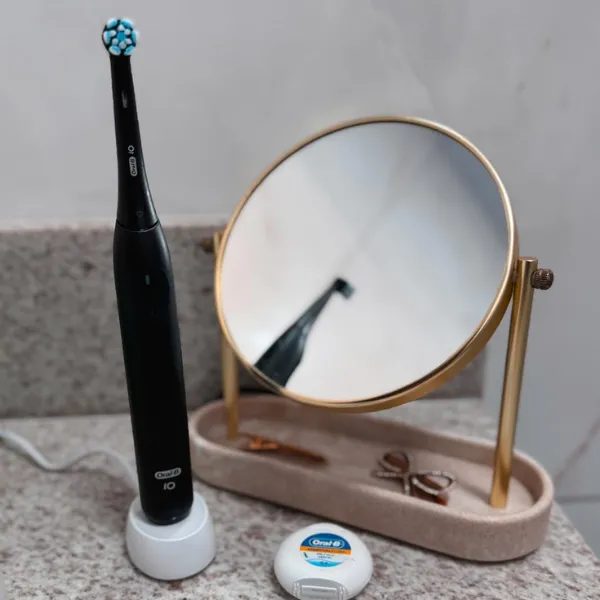 Escova elétrica Oral-B iO Series 2 com base carregadora ao lado de espelho de bancada e fio dental Oral-B