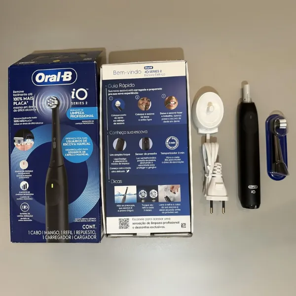 Conteúdo da embalagem da escova elétrica Oral-B iO Series 2 organizado sobre a superfície: aparelho, refil, manual e carregador