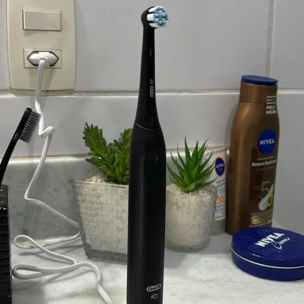 Escova elétrica Oral-B iO Series 2 sobre pia de banheiro ao lado de itens de cuidados pessoais e plantas decorativas